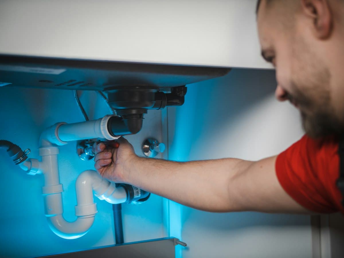A tradesperson working on pipes under a sink